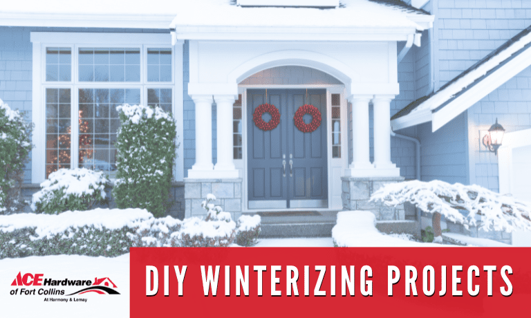 DIY Winterizing Projects text over a snow covered entrance to a home. The home has two blue doors with red wreaths, and snow covered shrubs.