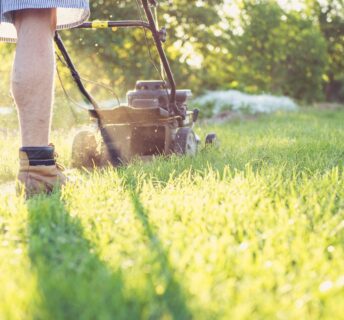 Photo of man mowing lawn. Keep Your Lawn Lush and Green in July.